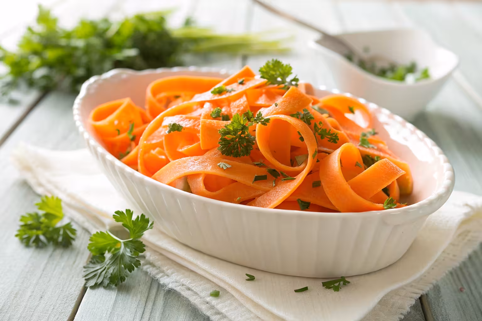 A vibrant carrot ribbon salad in a white bowl, tossed with a zesty vinaigrette and fresh parsley.